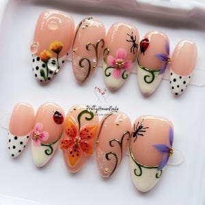 May include: A set of ten press-on nails with a nude base, featuring hand-painted designs including yellow and orange flowers, ladybugs, ants, black polka dots, and gold swirls. The text Pretty House Nails Love Life Design is printed in the center.