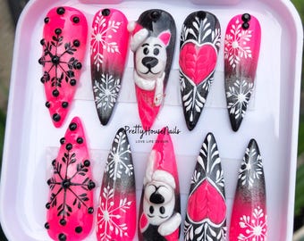 May include: A set of ten pink and black Christmas-themed false nails with snowflake and heart designs. The nails feature a white snowman with a black hat and a pink heart.
