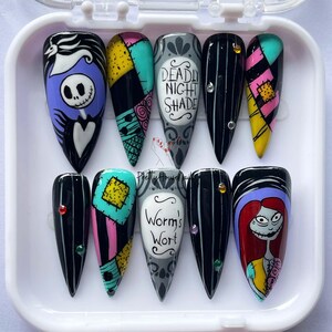 May include: A set of ten long, pointed false nails with designs inspired by "The Nightmare Before Christmas." The nails feature characters like Jack Skellington and Sally, along with patchwork and striped patterns in black, white, and various colours.