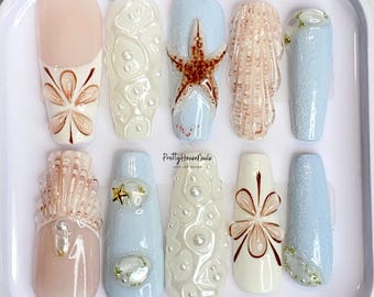 May include: Set of ten false nails with a beach theme. The nails are decorated with seashells, starfish, pearls, and flowers. The nails are in a white plastic case with the text "PrettyHouseNails LOVE LIFE DESIGN".
