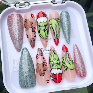 May include: A set of ten false nails with a Christmas theme. The nails are decorated with glitter, gingerbread men, candy canes, and the Grinch. The nails are in a clear plastic case with the text "PrettyHouseNails" and "Love Life Design".