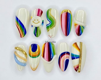 May include: Ten white oval-shaped fake nails with different rainbow designs. Some nails have a smiley face, a swirl, and a gold stripe.