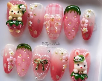 May include: Pink and green nail art with a strawberry, a bow, a flower, and a bunny design. The nail art is on a white background. PrettyHouseNails LOVE LIFE DESIGN.