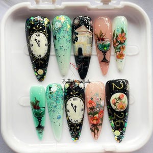 May include: A set of ten long, pointed artificial nails with various designs. The designs include clocks, buildings, floral arrangements, and glitter. The nails are in a white plastic container. The nail art is colorful and detailed.
