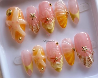 May include: A set of ten artificial nails with a beach theme. The nails feature a variety of designs, including starfish, seashells, and floral accents. The color palette includes shades of pink, yellow, and gold. The text "Pretty House Nails Love Life Design" is visible.
