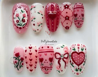 May include: A set of ten artificial nails with various designs. The nails feature pink, red, and white colors with floral, heart, and bow patterns. The text "Pretty House Nails LOVE LIFE DESIGN" is visible.