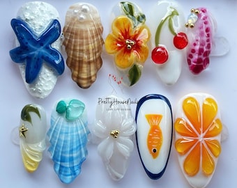 May include: Ten different nail designs featuring summer themes. The designs include a starfish, seashells, a flower, cherries, a fish, an orange slice, and a palm tree.  The designs are painted on white oval-shaped nail tips.