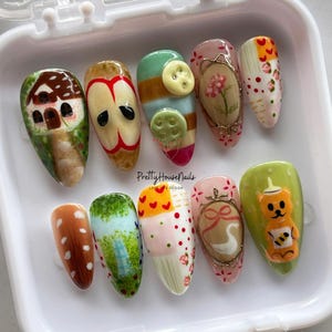Juego de uñas con diseño de naturaleza caprichosa con oso, manzana, botones y flores. Uñas postizas artesanales de estilo cottagecore, uñas festivas y uñas kawaii.