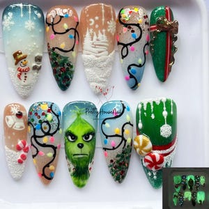 May include: A set of ten artificial nails with festive Christmas designs. The nails feature a snowman, Christmas lights, winter scenes, and Grinch-themed art. Some nails have glitter and 3D elements. The nails glow in the dark.