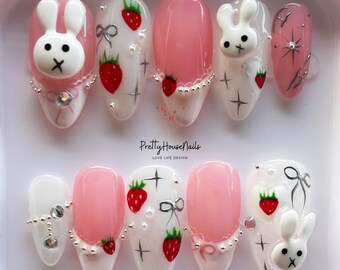 May include: Set of pink and white false nails with a strawberry and bunny design. The nails have a glossy finish and are decorated with rhinestones and silver glitter.