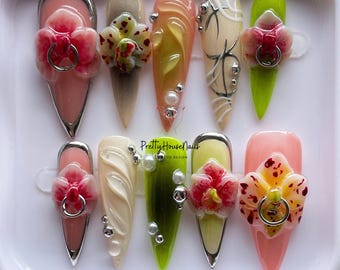 May include: Set of ten false nails with a pink, green, and white base. Each nail is decorated with a 3D orchid flower and rhinestones. The nails are arranged in a white display case with the text "PrettyHouseNails" and "LOVE LIFE DESIGN".