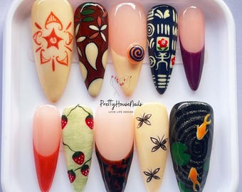 May include: A set of ten artificial nails in a white plastic case. The nails feature various designs, including floral patterns, strawberries, butterflies, and koi fish. The nails are painted in a variety of colors, including beige, red, and black. The text "Pretty House Nails" is visible.