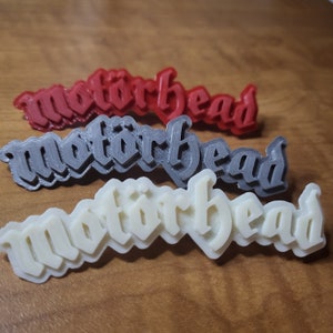 May include: Three 3D printed versions of the word "Motorhead" in red, gray, and white.