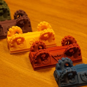 Pode incluir: Seis ba&uacute;s em miniatura coloridos com al&ccedil;as em forma de polvo. Os ba&uacute;s est&atilde;o dispostos em fila da esquerda para a direita, com as cores que v&atilde;o do verde escuro ao azul. Cada ba&uacute; tem um design diferente na parte frontal.