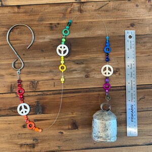 May include: A rainbow-colored beaded wind chime with peace signs and a silver bell. The beads are red, orange, yellow, green, blue, and purple.
