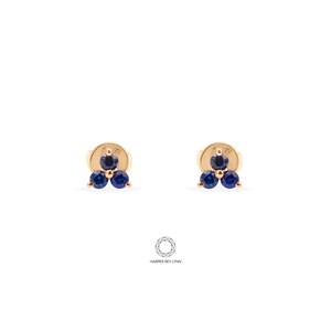 May include: A pair of gold earrings with three blue sapphire stones each. The earrings are small and delicate.