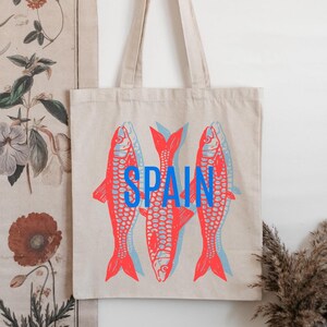 May include: A white canvas tote bag with red and blue fish illustrations and the word "SPAIN" printed in blue.