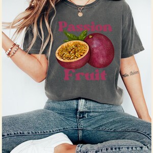 May include: A grey t-shirt with a graphic of a passion fruit and the text "Passion Fruit" in pink letters.