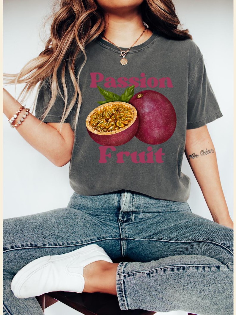 May include: A grey t-shirt with a graphic of a passion fruit and the text "Passion Fruit" in pink letters.