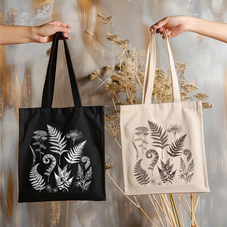 May include: Two tote bags with black and white fern illustrations. The bag on the left is black with white ferns. The bag on the right is beige with black ferns.
