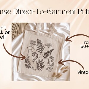 May include: A white canvas tote bag with a black and white fern print. The bag is made with direct-to-garment printing, which is rated for 50+ washes and gives a vintage look. The text "won't crack or peel!" is written on the left side of the image.