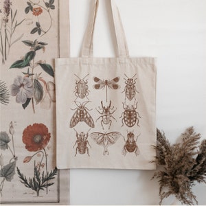 May include: A beige tote bag with brown insect illustrations. The insects include beetles, butterflies, and moths. The bag has a brown canvas strap.