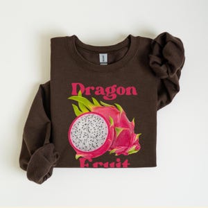 May include: Brown sweatshirt with a pink and white dragon fruit graphic and the text "Dragon Fruit" in pink.