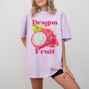May include: A lavender t-shirt featuring a graphic of a dragon fruit and the text "Dragon Fruit" in pink.