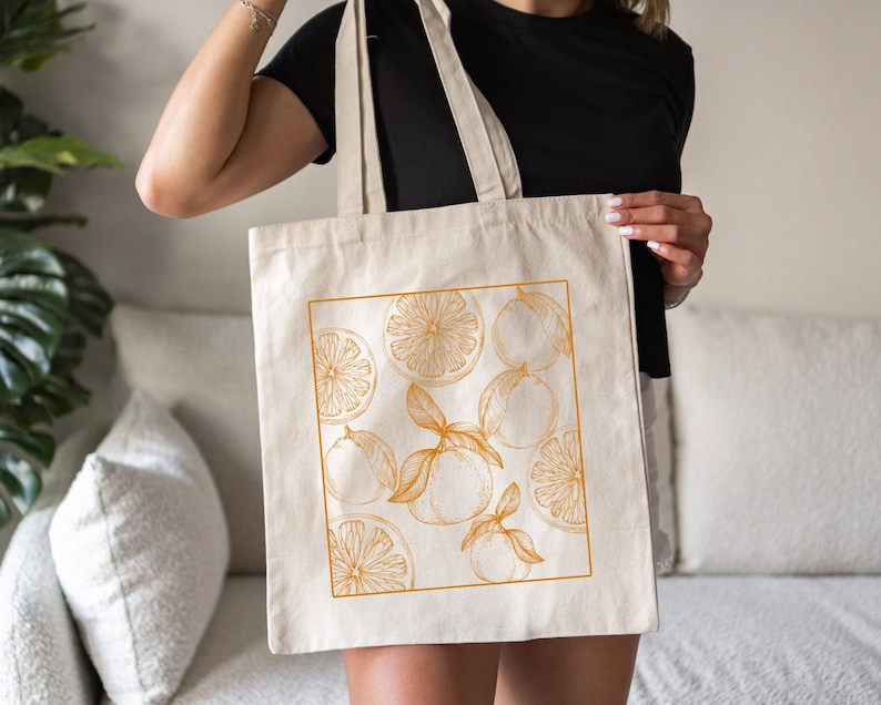 May include: A white canvas tote bag with a design of orange slices and leaves in a gold color.