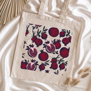 May include: A beige tote bag with a red pomegranate pattern. The bag has two handles and is made of canvas.