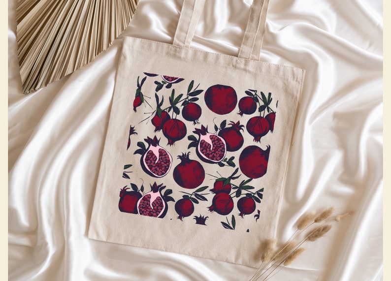May include: A beige tote bag with a red pomegranate pattern. The bag has two handles and is made of canvas.