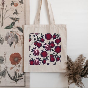 May include: A beige tote bag with a red and white pomegranate print. The bag has a long handle and is made of canvas.