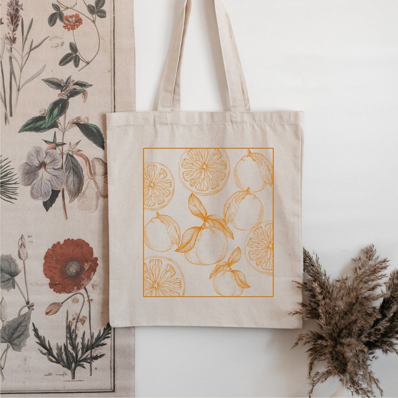 May include: A beige tote bag with a pocket on the front. The pocket features a graphic of orange slices in an orange outline.