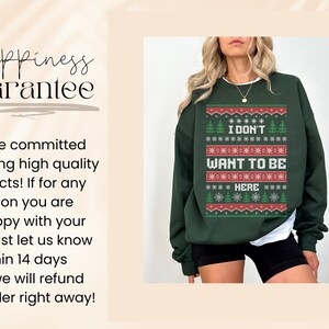 K&ouml;nnte beinhalten: Dunkelgr&uuml;nes Sweatshirt mit weihnachtlichem Design. Der Text "I DON'T WANT TO BE HERE" ist in Wei&szlig; und Rot dargestellt. Das Design beinhaltet Schneeflocken und Weihnachtsb&auml;ume. Das Sweatshirt wird mit schwarzen Shorts getragen.
