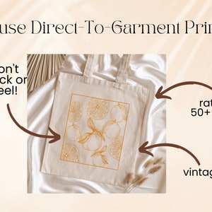 May include: A white tote bag with a design of orange slices and leaves printed in a light orange color. The text "We use Direct-To-Garment Printing" is at the top of the image. The text "won't crack or peel!" is on the left side of the image. The text "rated for 50+ washes" is on the right side of the image. The text "vintage look" is at the bottom right of the image.