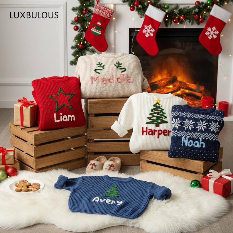 May include: A collection of personalized Christmas sweaters in various colors, including red, white, and blue. Each sweater features a name and festive design, such as a star, Christmas tree, or snowflakes. The sweaters are displayed on wooden crates and a fluffy white rug.