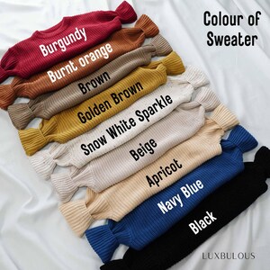 May include: A stack of ten sweaters in different colors, including burgundy, burnt orange, brown, golden brown, snow white sparkle, beige, apricot, navy blue, and black. The sweaters are arranged from darkest to lightest, with the burgundy sweater on top and the black sweater on the bottom. The text "Colour of Sweater" is written in white letters on a black background at the top of the image.