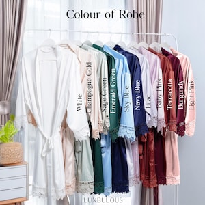 Op de afbeelding: Een display van satijnen badjassen in diverse kleuren, waaronder wit, champagne goud en marineblauw, hangend aan een rek. Elke badjas heeft kanten afwerking en is gelabeld met de kleur. De tekst "Colour of Robe" staat bovenaan en de merknaam "LUXBULOUS" onderaan.