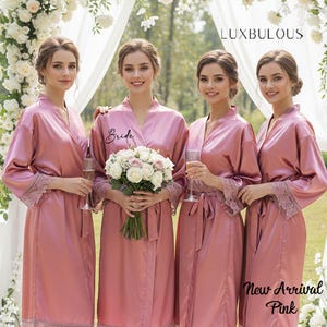 Könnte beinhalten: Vier Frauen in passenden, staubrosafarbenen Satin-Roben mit Spitzensaum. Eine Robe ist mit "Bride" beschriftet. Die Roben haben ein Wickeldesign und sind an der Taille gebunden. Der Text "New Arrival Pink" und "Luxbulous" ist enthalten.
