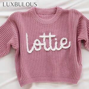 May include: A pink knitted jumper with the name "Lottie" embroidered in white yarn.