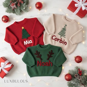 May include: Three personalized Christmas sweaters in red, cream, and green. The red sweater has a green tree and the name "Mia". The cream sweater has a green tree and the name "Corbin". The green sweater has brown antlers and the name "Noah".