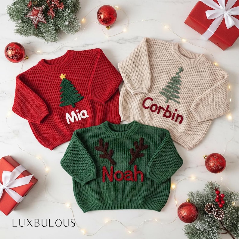 May include: Three personalized Christmas sweaters in red, cream, and green. The red sweater has a green tree and the name "Mia". The cream sweater has a green tree and the name "Corbin". The green sweater has brown antlers and the name "Noah".