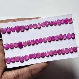 Pode incluir: Três fileiras de pedras preciosas rosa facetadas de várias formas, incluindo ovais, lágrimas e cortes geométricos, são exibidas em um cartão branco. As pedras são dispostas em linha, mostrando sua cor e clareza.