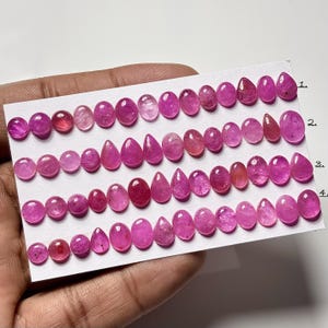 Puede incluir: Una colección de gemas rosas, incluyendo formas ovaladas y de lágrima, dispuestas sobre una tarjeta blanca. Las gemas varían en tonalidad, desde rosa claro hasta magenta intenso. La tarjeta está numerada del 1 al 4.