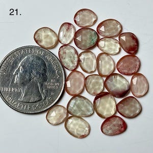 Op de afbeelding: Een verzameling gefacetteerde, ovaalvormige edelstenen in tinten perzik, crème en rood. Een Amerikaanse kwart dollar munt is inbegrepen ter referentie. De edelstenen zijn doorschijnend met diverse interne patronen. Het nummer "21" staat linksboven.