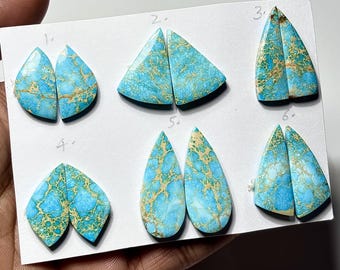 May include: Six pairs of polished turquoise and gold-colored gemstone cabochons, each with a unique shape. The stones are arranged on a white card, showcasing their intricate patterns and natural beauty. Ideal for jewelry making or collecting.