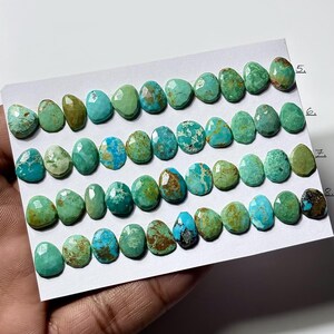 May include: A collection of faceted, teardrop-shaped turquoise gemstones arranged in five horizontal rows on a white card. The stones display various shades of blue and green with natural brown matrix patterns, numbered 5, 6, 7, and 8.