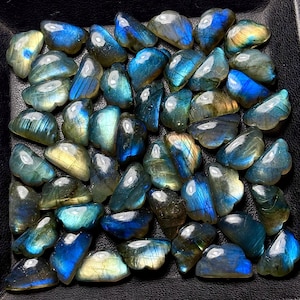 Pode incluir: Uma coleção de pedras preciosas de labradorite polidas. As pedras exibem uma gama de cores, incluindo azuis, verdes e amarelos, com flashes iridescentes. As pedras preciosas são de forma irregular e parecem ter sido polidas.