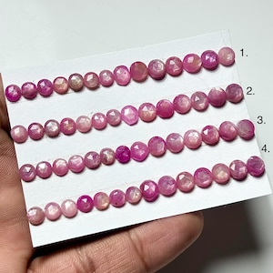 Könnte beinhalten: Vier Reihen facettierter, rosa Edelsteine werden auf einer weißen Karte präsentiert. Die Edelsteine variieren in Größe und Farbton, von hellrosa bis tiefmagenta. Die Edelsteine sind linear angeordnet und zeigen ihre polierten Oberflächen.