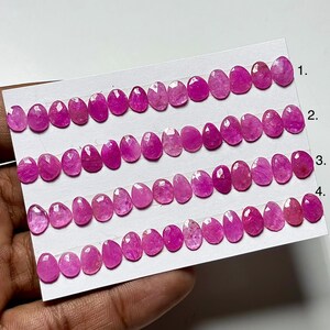 May include: Rows of oval-shaped, faceted pink gemstones are arranged on a white card. The gemstones vary slightly in color and clarity, with a vibrant, saturated pink hue. The card is labeled with numbers 1 through 4, indicating different rows of stones.